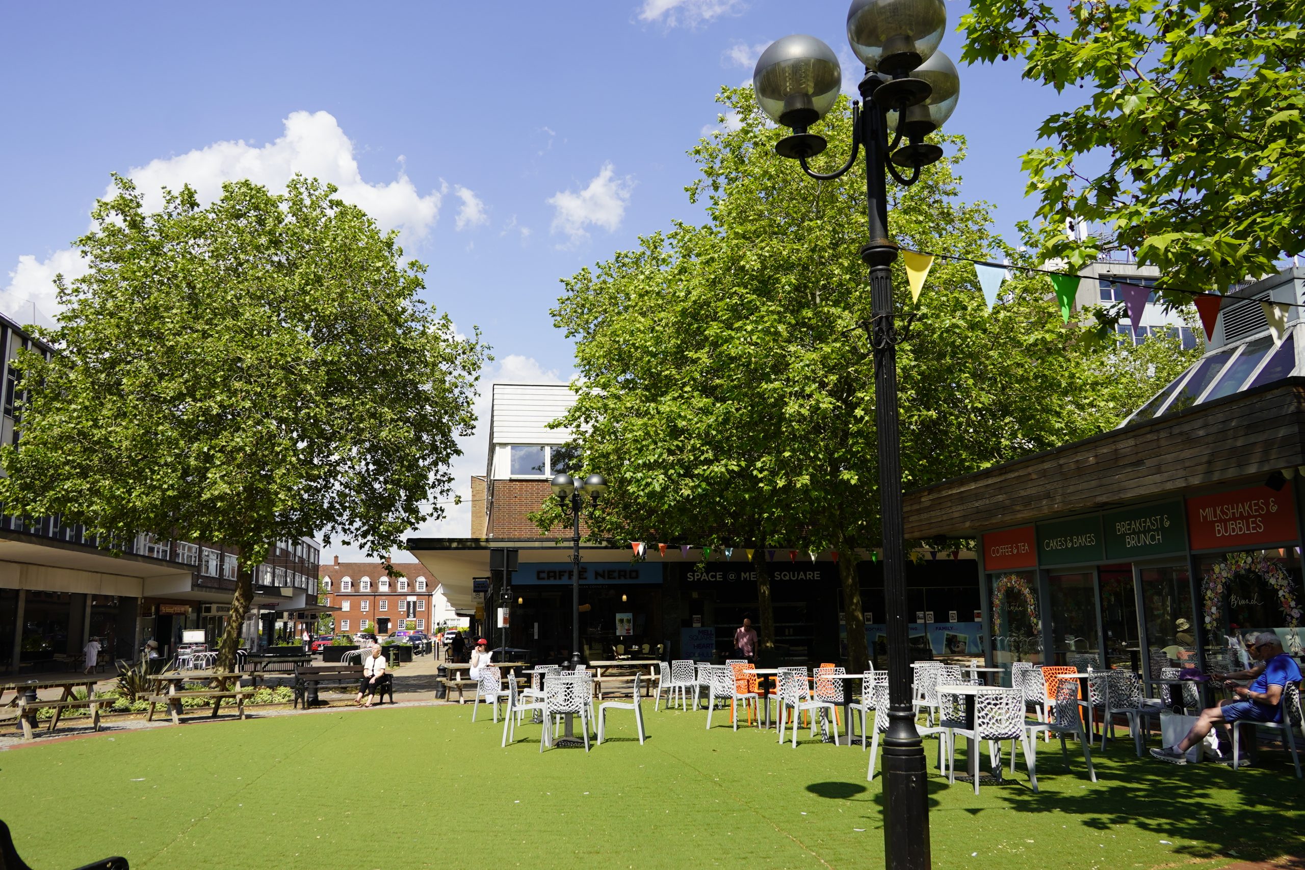 A sunny day in Mell Square, looking towards Mill Lane and Warwick Road through the lush green trees.